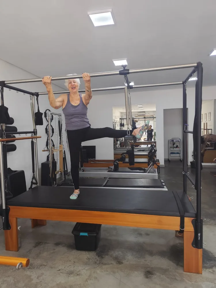 Aluna da terceira idade sorrindo durante exercício de equilíbrio e mobilidade no Cadillac, em aula de Pilates Clássico no Espaço Vitafit Pilates, em Vila Brasília, Aparecida de Goiânia